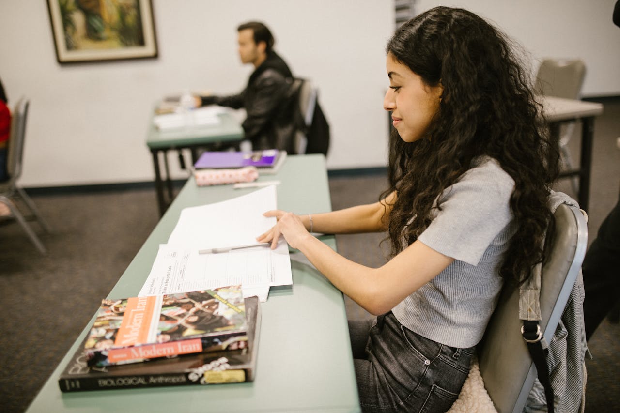 Young woman focused on exam preparations in a college classroom, writing notes on test papers.